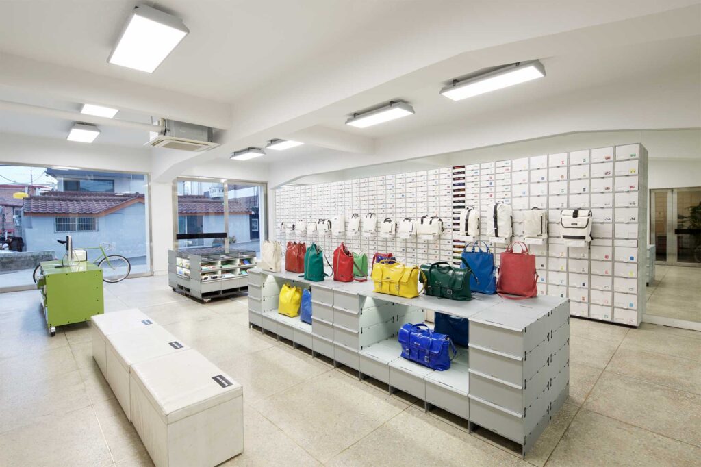 View of Freitag MMMG Seoul, South Korea, store from an angle, with black and white bags in minimalist display on right background and vibrant colorful bags in foreground.