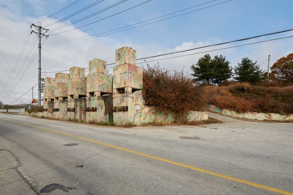 Autumn-colored bushes flourish beside demolition barriers lining a rural road along the former civilian control line near the Korean Demilitarized Zone in South Korea.