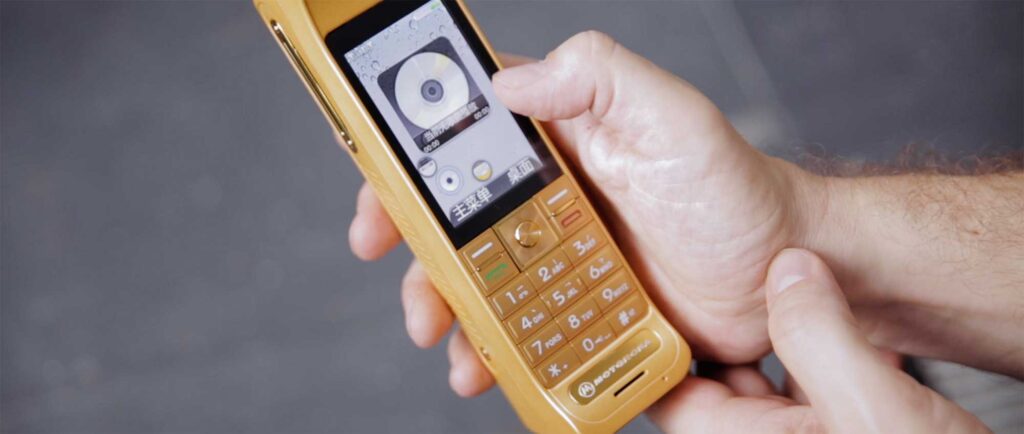 In a cell phone shop in Shenzhen, China, an old-style bulky beige cell phone features a retro display showcasing an MP3 disc player.