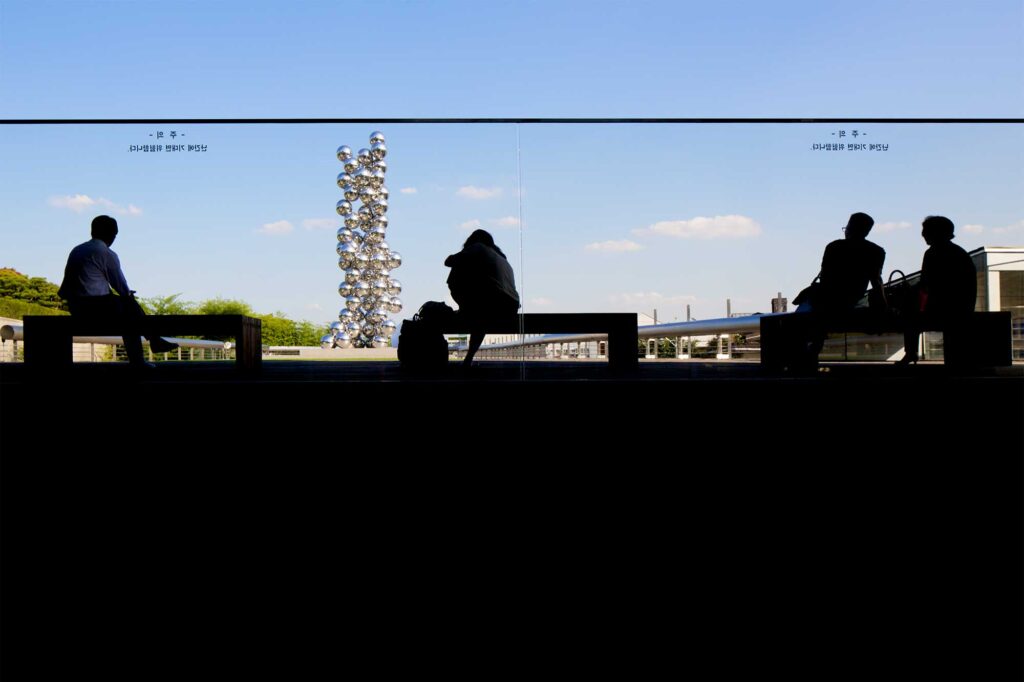 Visitors at Leeum, Samsung Museum of Art in Seoul, South Korea, silhouetted against Anish Kapoor's "Tall Tree and the Eye" sculpture in the background.