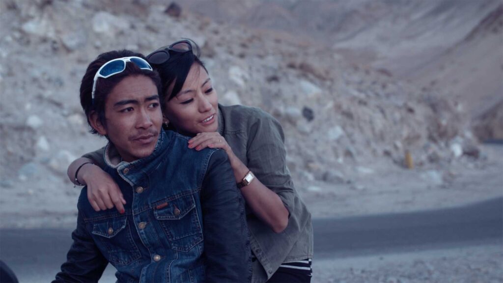 A cool young man from Leh, Ladakh, India, confidently rests on his motorbike while his girlfriend clings to him on the backseat.