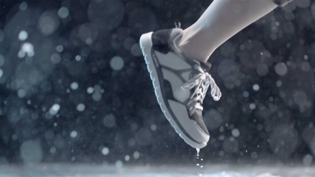 A right foot lifts off a wet surface, surrounded by illuminated water particles against a dark background for the Millet sports fashion campaign.