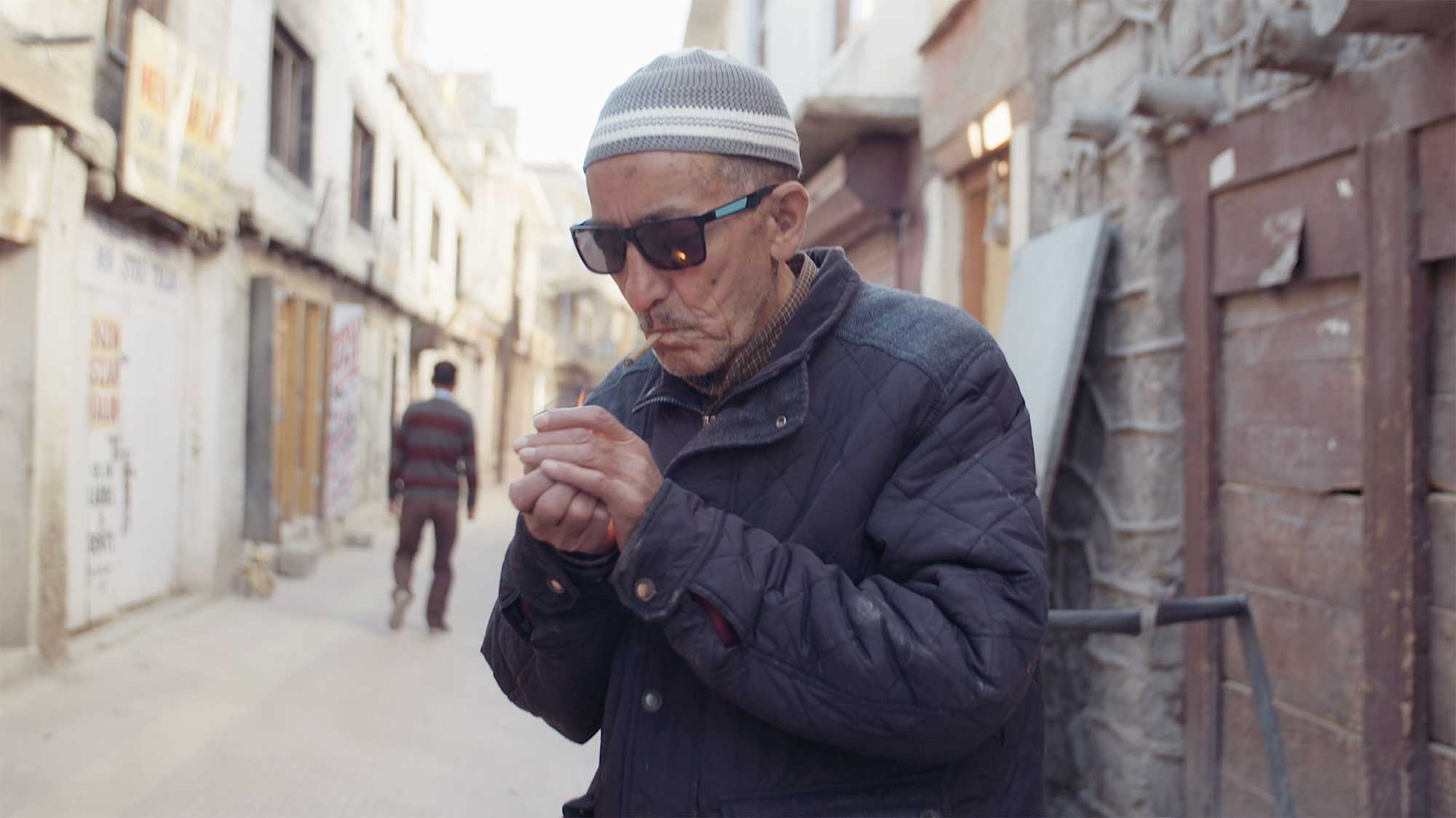 An older man lights himself a smoke in an alleyway outside of his home in Leh, Ladakh, India.