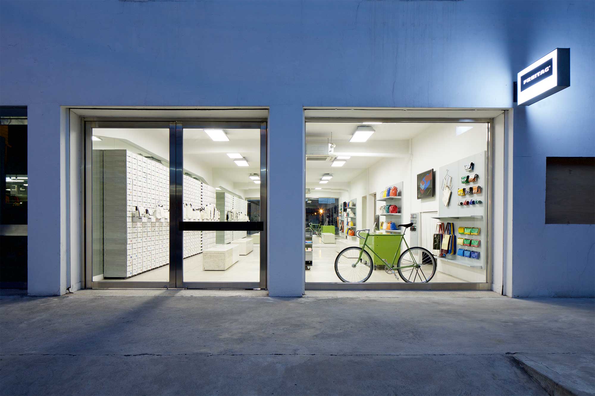 Exterior view at dusk of Freitag MMMG Seoul, South Korea, showcasing minimalist displays and furniture featuring a vibrant range of colorful bags.