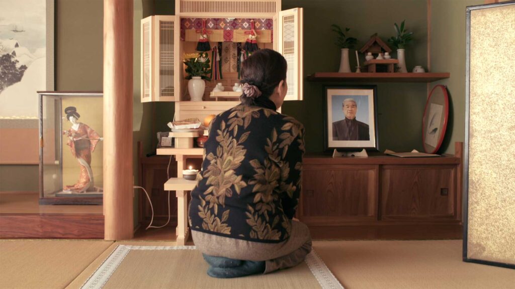 An elderly Japanese Takeshima activist sits in front of a small shrine at home dedicated to her late husband, following in his footsteps to continue Takeshima activism for the film This Island is Ours.