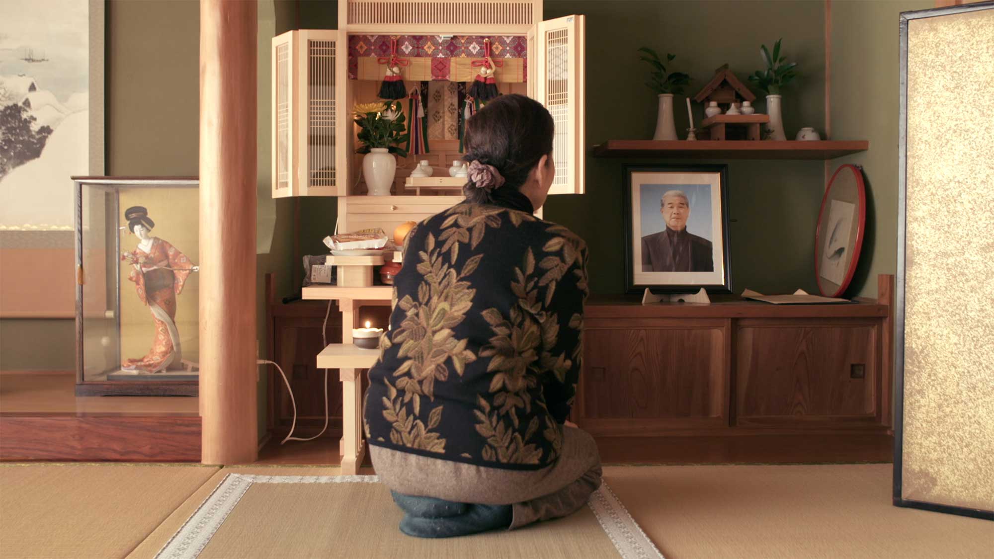 An elderly Japanese Takeshima activist sits in front of a small shrine at home dedicated to her late husband, following in his footsteps to continue Takeshima activism for the film This Island is Ours.