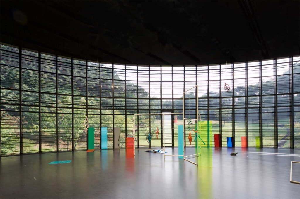 SUPER-SPREADER MEDIA VIRUS exhibition in atrium of Nam June Paik Art Center, Seoul, South Korea, features various installation artworks against wide open round-shaped glass facade dividing exhibition space from museum garden.