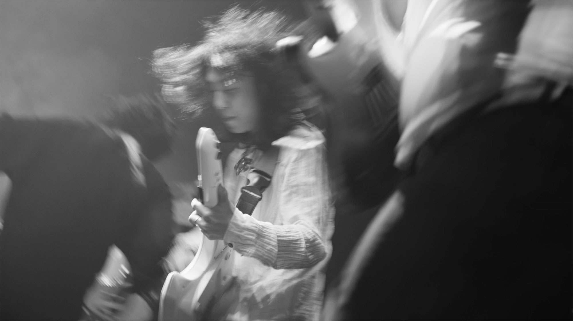 Young Korean guitarist on stage with his band giving wild performance in Seoul, South Korea, for music video "Beautiful Woman" from Tune-Up Joong-Hyun Shin: Origin tribute album.