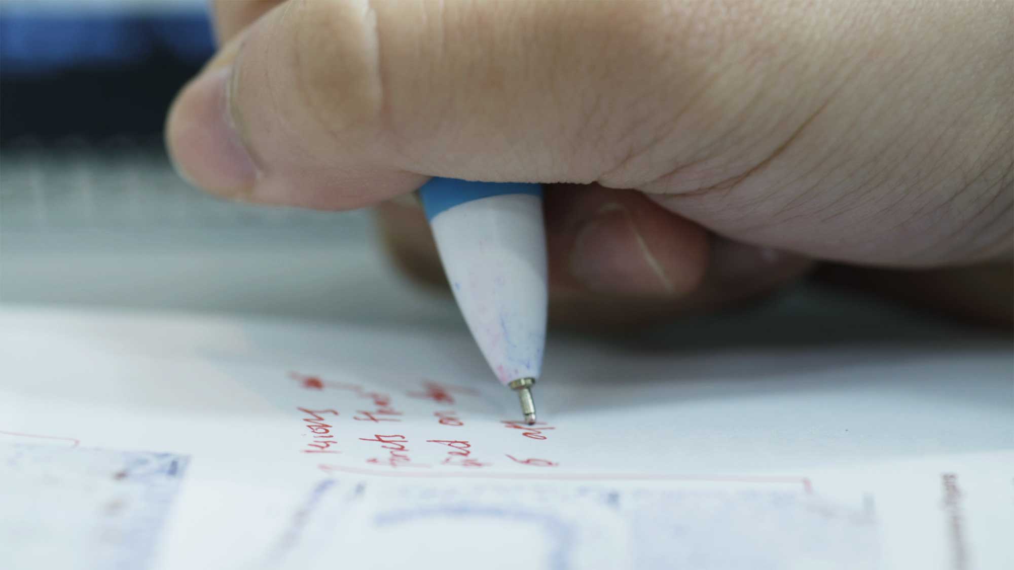 Close-up of hand and pen of Minerva University student taking notes while listening to class online in cafe in Seoul, South Korea.