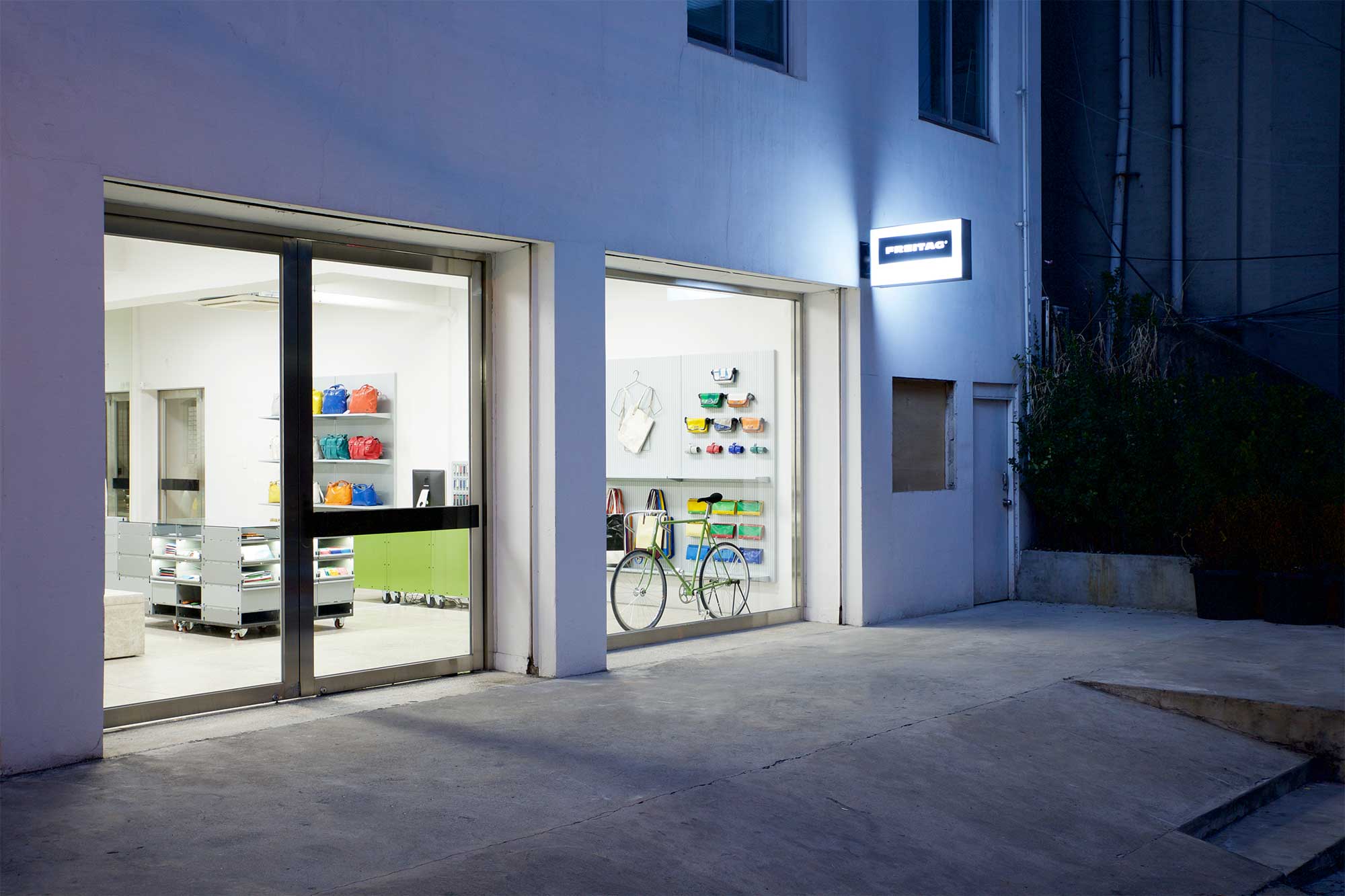 Exterior view at dusk from an angle of Freitag MMMG Seoul, South Korea, highlighting minimalist displays and furniture with a vibrant range of colorful bags.