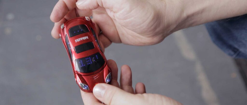 In a cell phone shop in Shenzhen, China, a striking red cellphone shaped like a Ferrari, featuring the logo on the roof, showcases its unique design.