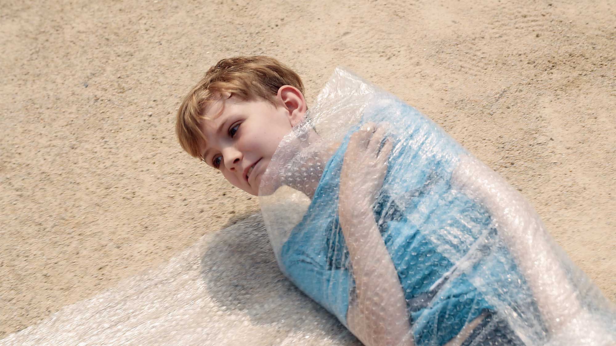 Young boy on sandy floor wraps himself in bubble wrap for short film IF, where children explore meaning of space and architecture.