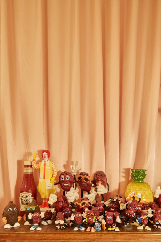 A collection of whimsical puppets and comic characters perched on a window sill beneath a curtain in a small shop in Seoul, South Korea.