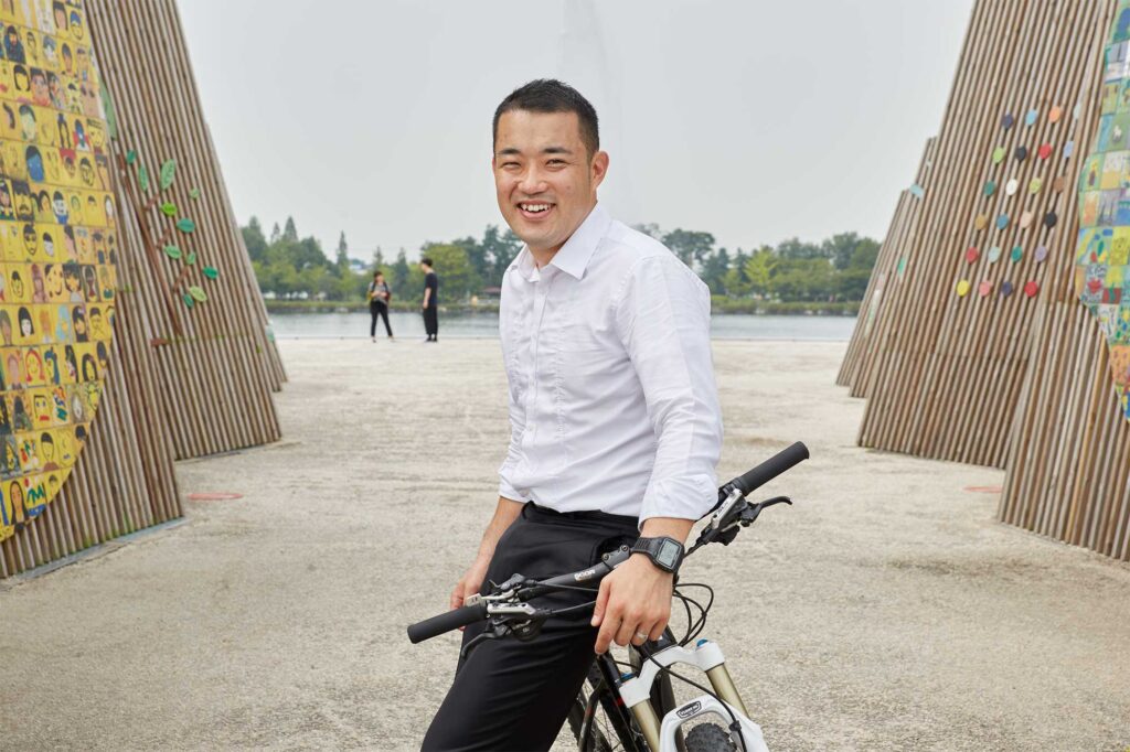 Portrait of Lee Jaeyong, an urban mountain bike trickster, casually leaning on his mountain bike in his office attire in Seoul, South Korea.