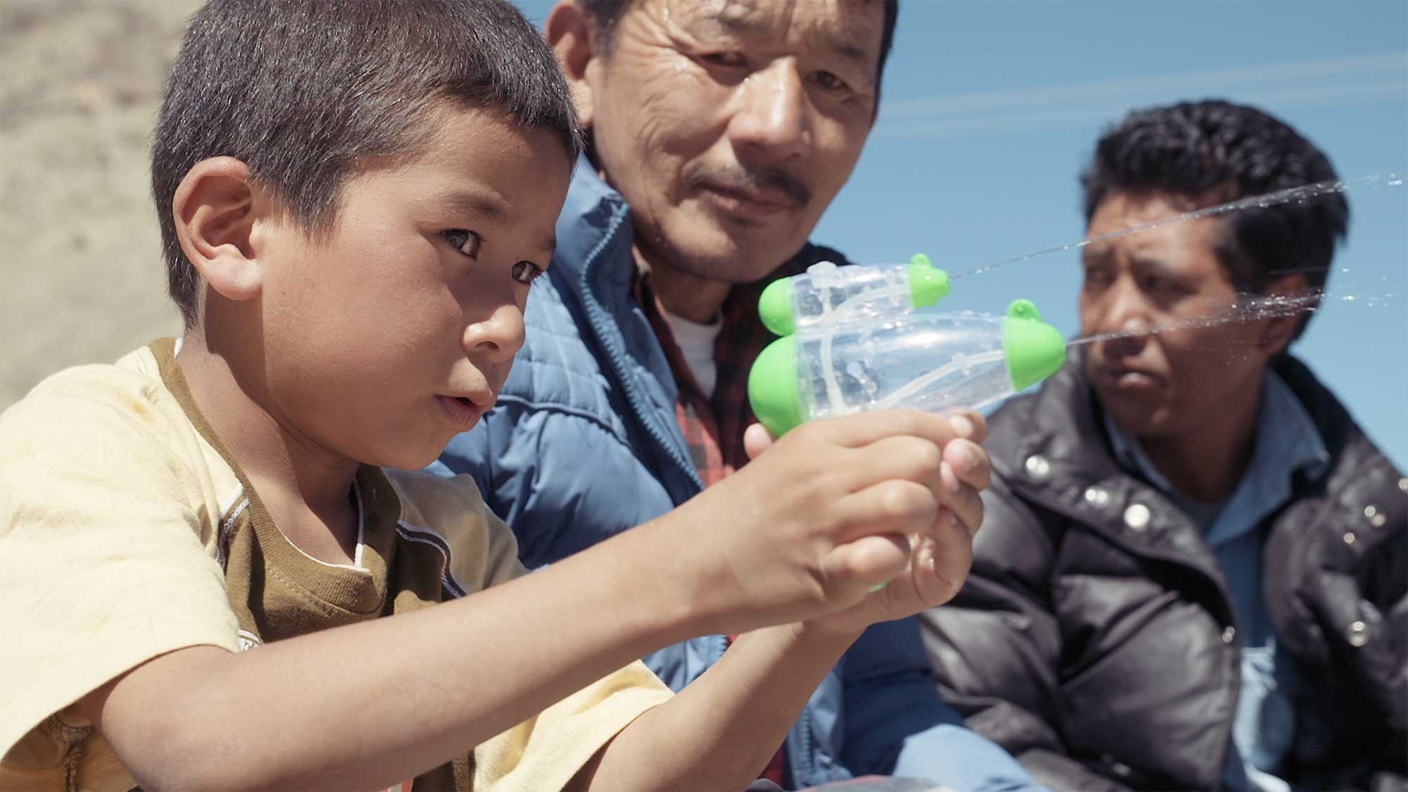 A young kid with a water pistol and his dad at a large Buddhist festival in the countryside of Ladakh, India.