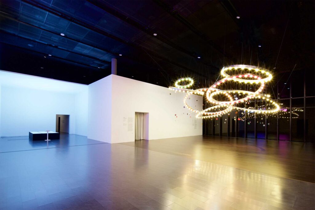 Mioon installation with circles of color and light in varying sizes hanging from dark ceiling and Euclid installation with large light box, part of SUPER-SPREADER MEDIA VIRUS exhibition, Nam June Paik Art Center, Seoul, South Korea.