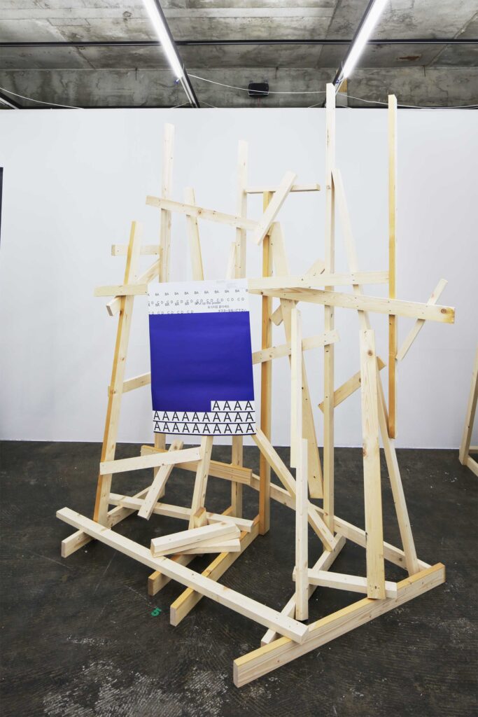 An abstract wooden construct adorned with a poster hanging down from one of the wooden bars, used as an installation piece for the poster exhibition in Seoul, South Korea, by Graphic Magazine as part of Propaganda Press.