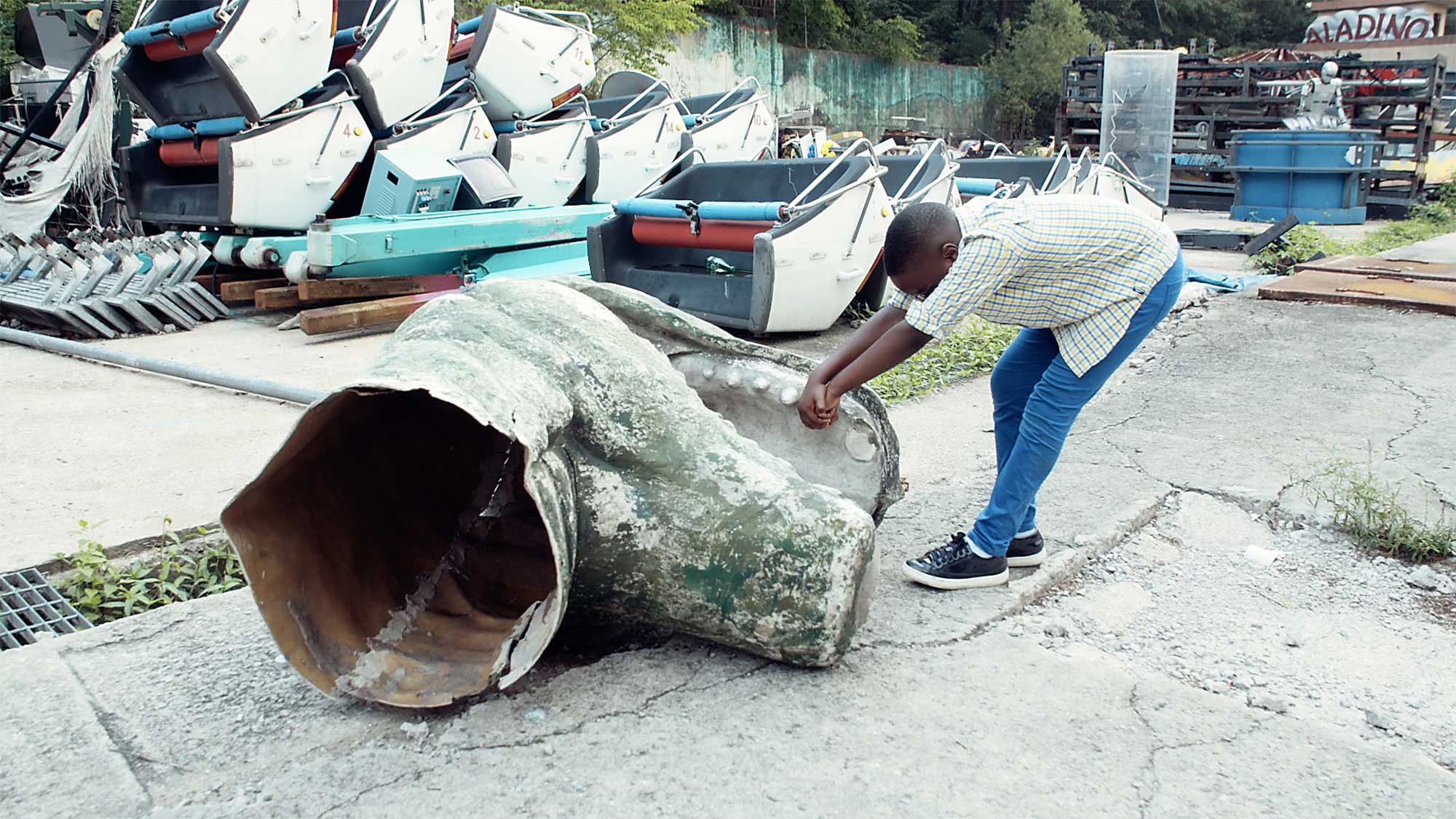 Young boy pulls big dinosaur head across pavement in abandoned fun-fair park in Seoul, South Korea, for short film IF, where children explore meaning of space and architecture.