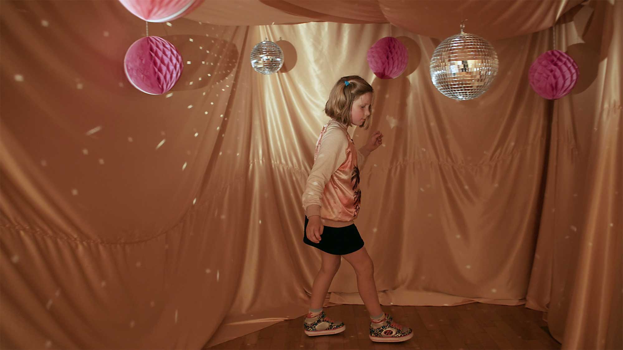 Young girl skates on rollable shoes inside secret cave made of golden blanket, with moody lighting reflecting off mirrorball and round paper structures in Seoul, South Korea, for short film IF.