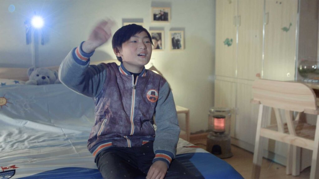 As part of a Western Union Chain of Betters campaign, a young Chinese boy sits on the edge of a bed in his newly decorated children's room in Changle District, China, speaking to his parents via a video call.