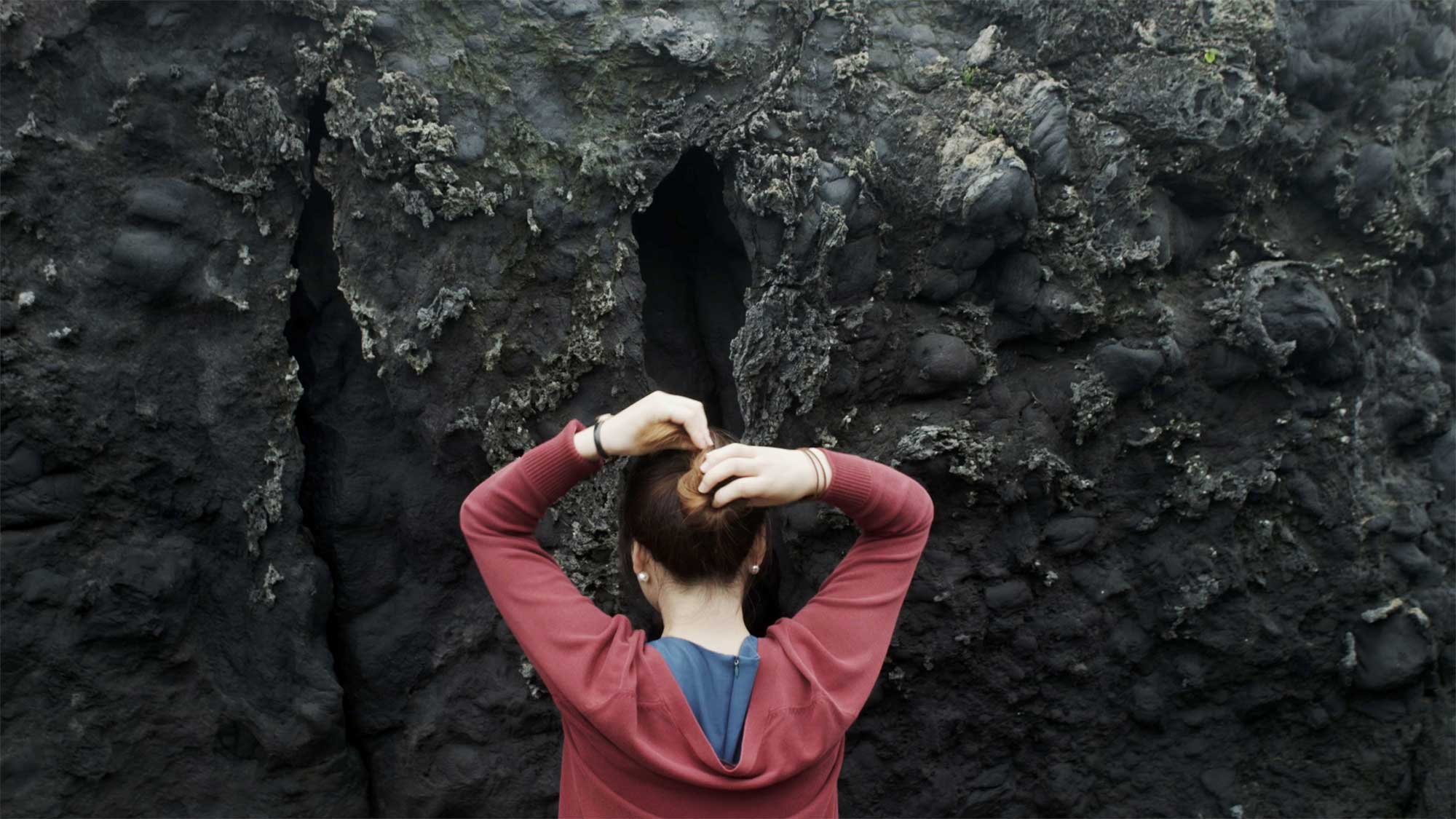 North korean female refugee ties long hair facing textured lava rock formation on Jeju Island South Korea