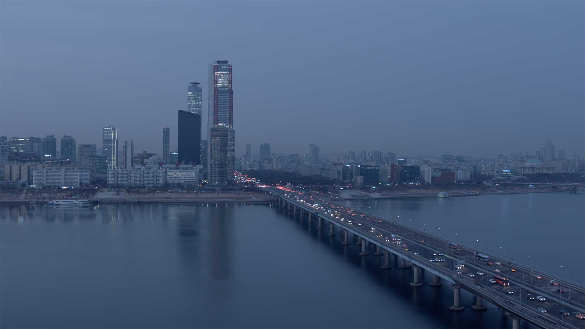 Early morning bridge traffic over Han River with Seoul skyline in haze.
