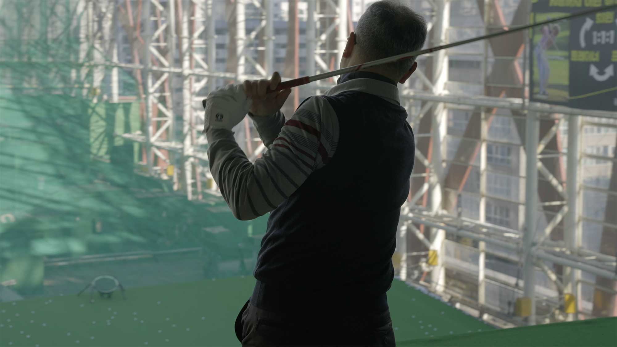 Man swings golf club at urban driving range in central Seoul.