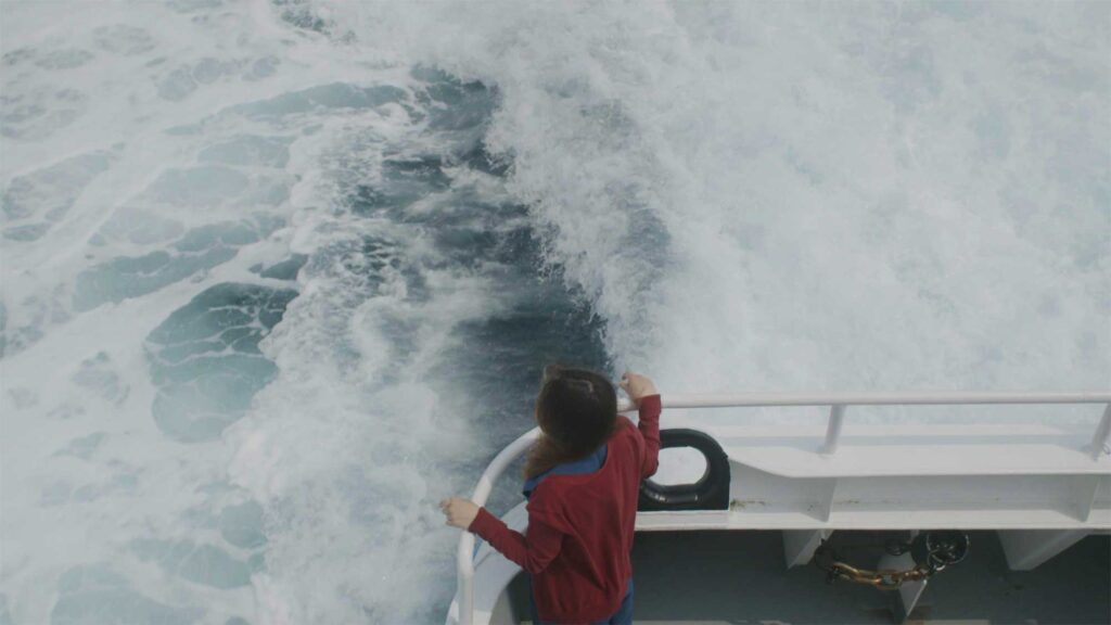 North korean female refugee stands on rear ferry platform to kapado gazing into churned white water behind boat near Jeju Island South Korea