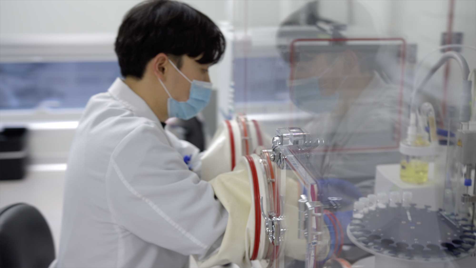 Scientist in lab coat and mask works in sterile chamber in Seoul lab.