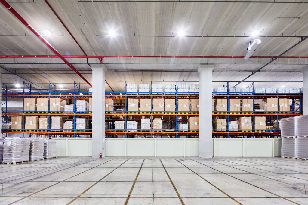 Warehouse interior with pallets stacked under bright lights.