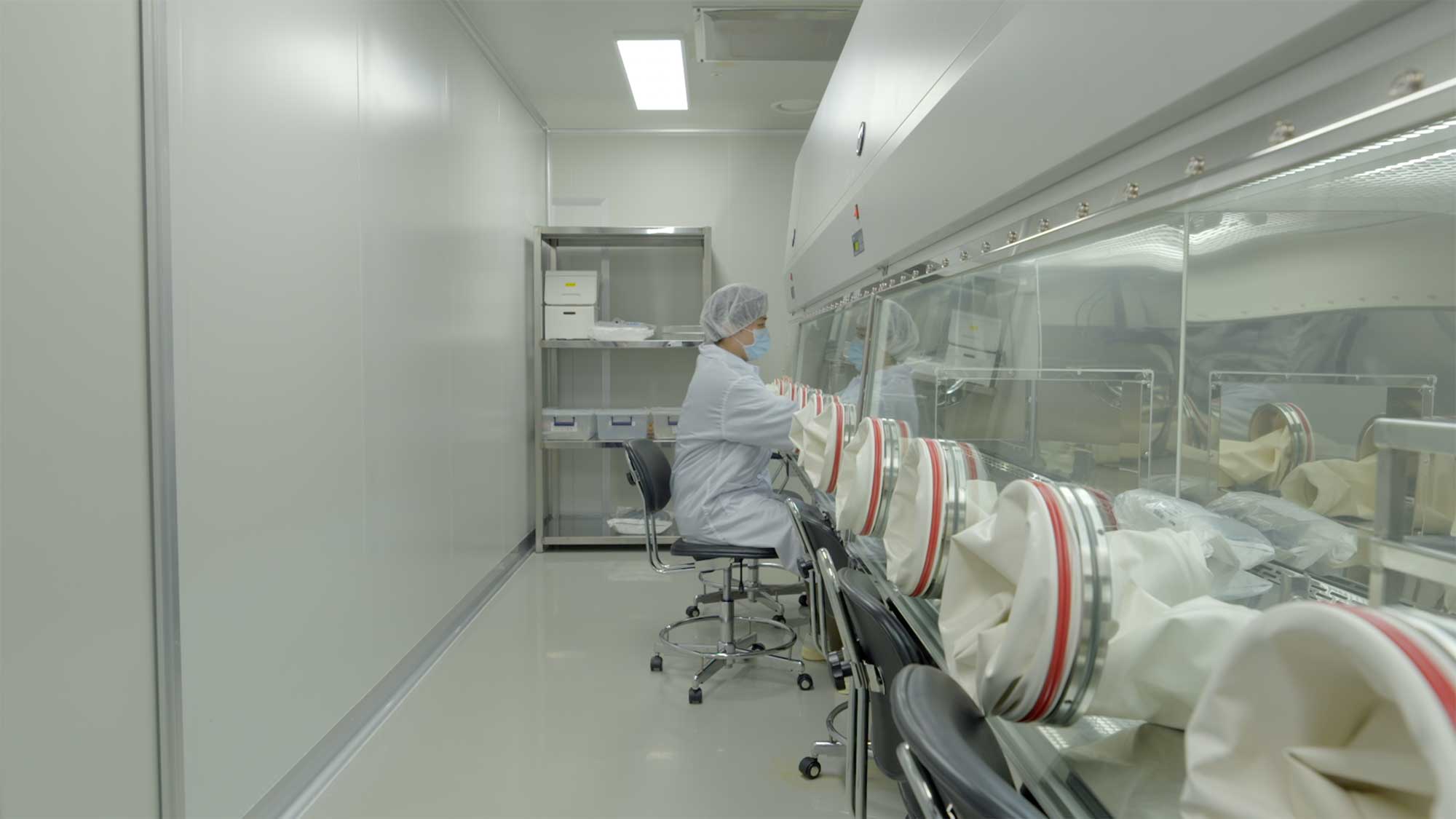 Scientist in lab works through sealed chamber with sensitive equipment.