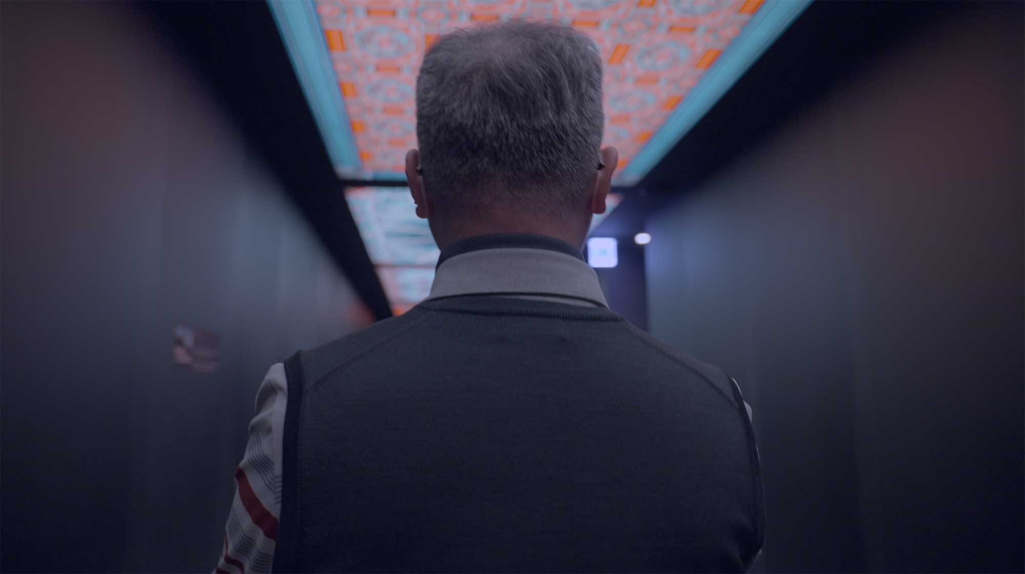 Exocobio CEO walks under LED mosaic ceiling toward elevator in Lotte Tower.