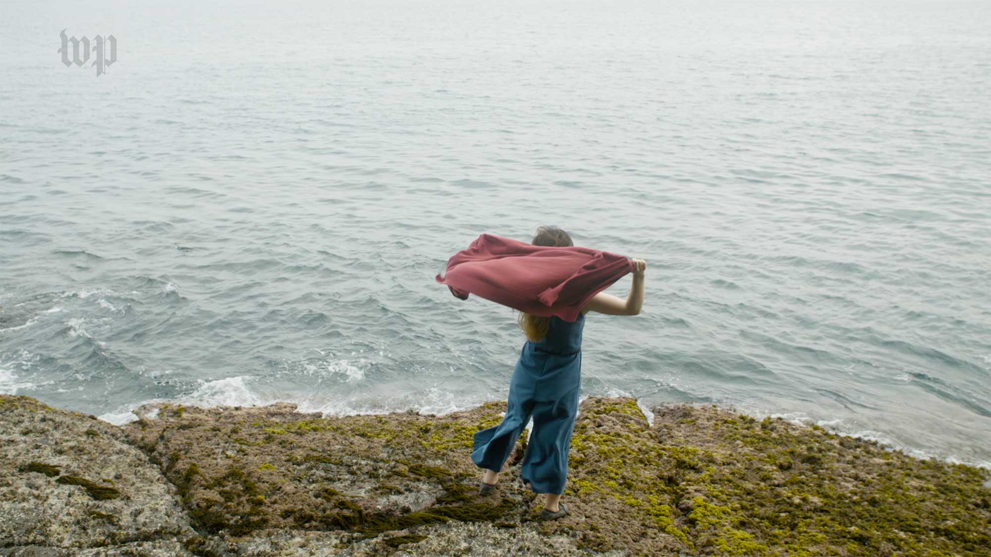North korean female refugee stands facing ocean holding up top blowing in the wind on southern coast of Jeju Island South Korea in yongmori