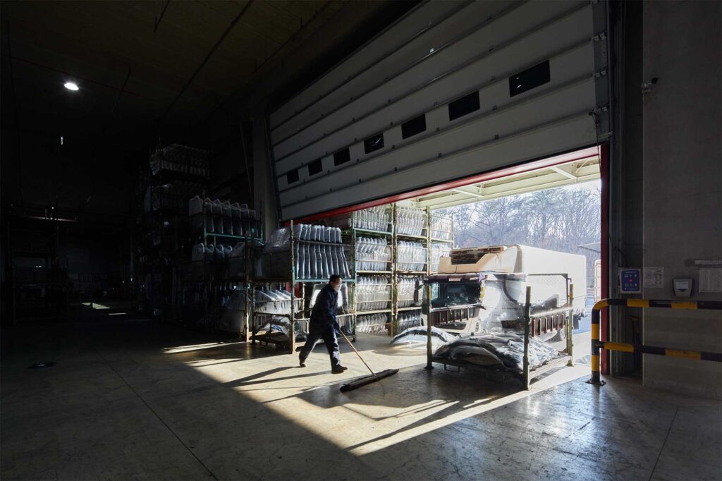 Worker sweeping warehouse floor in shadow-filled light.