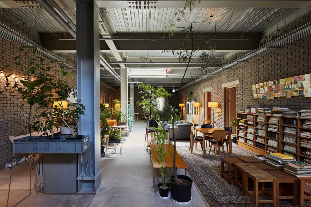Wide shot of hotel lounge in D&Department Jeju by Arario with seating areas divided by plants in bare concrete space.