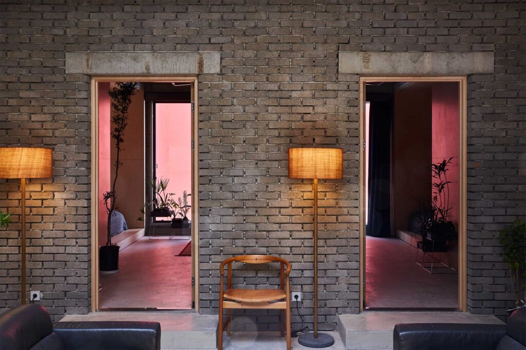 Shot from hotel lounge in D&Department Jeju by Arario showing two rooms through open door with red cast from neighboring buil.