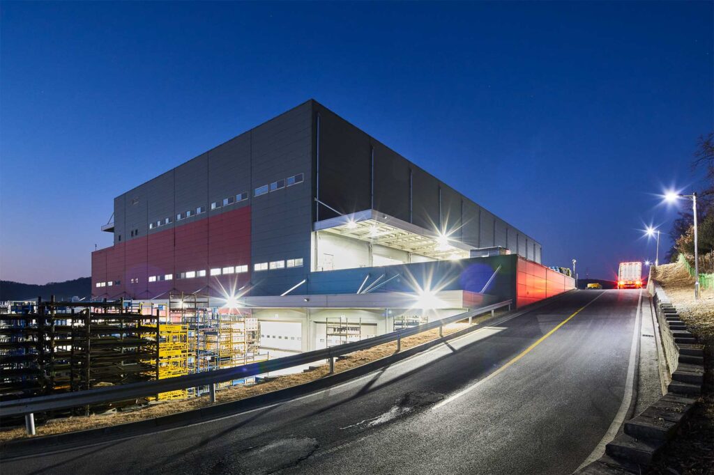 Lit logistics center exterior photographed at early night.