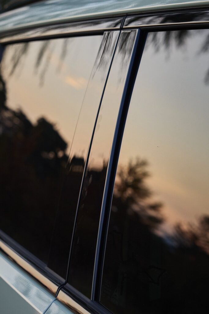 Kia EV3 side window and pillar reflecting landscape and evening sky.