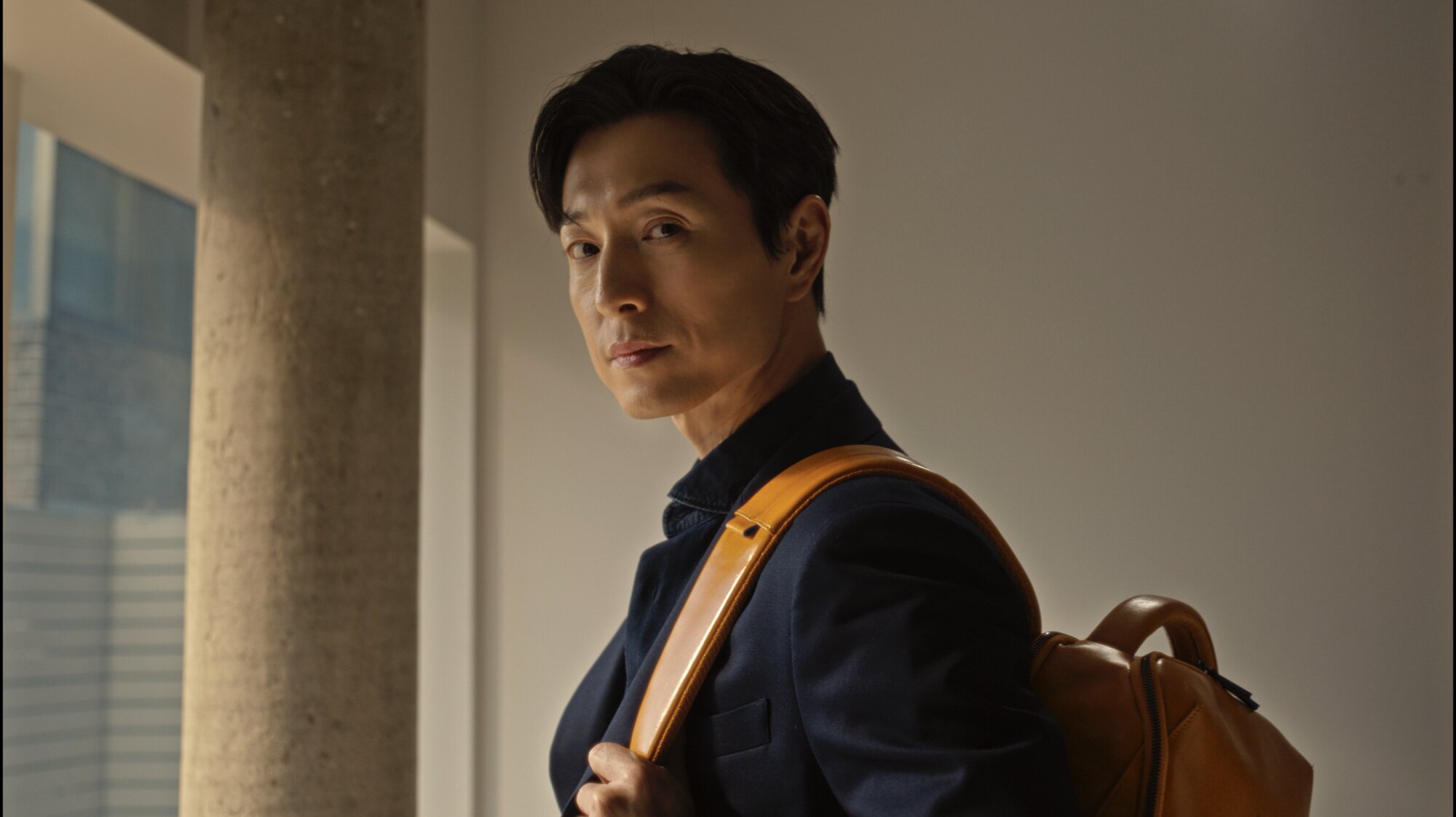 Jung Sung Il portrait holding Piquadro backpack strap in Seoul interior