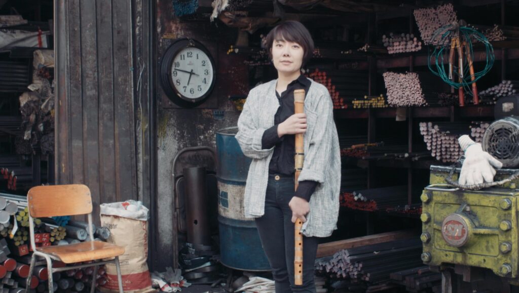 Korean musician Seungmin Cha holding traditional instrument inside metal workshop setting during Goethe Institut Seoul promo film focused on culture craft and sound