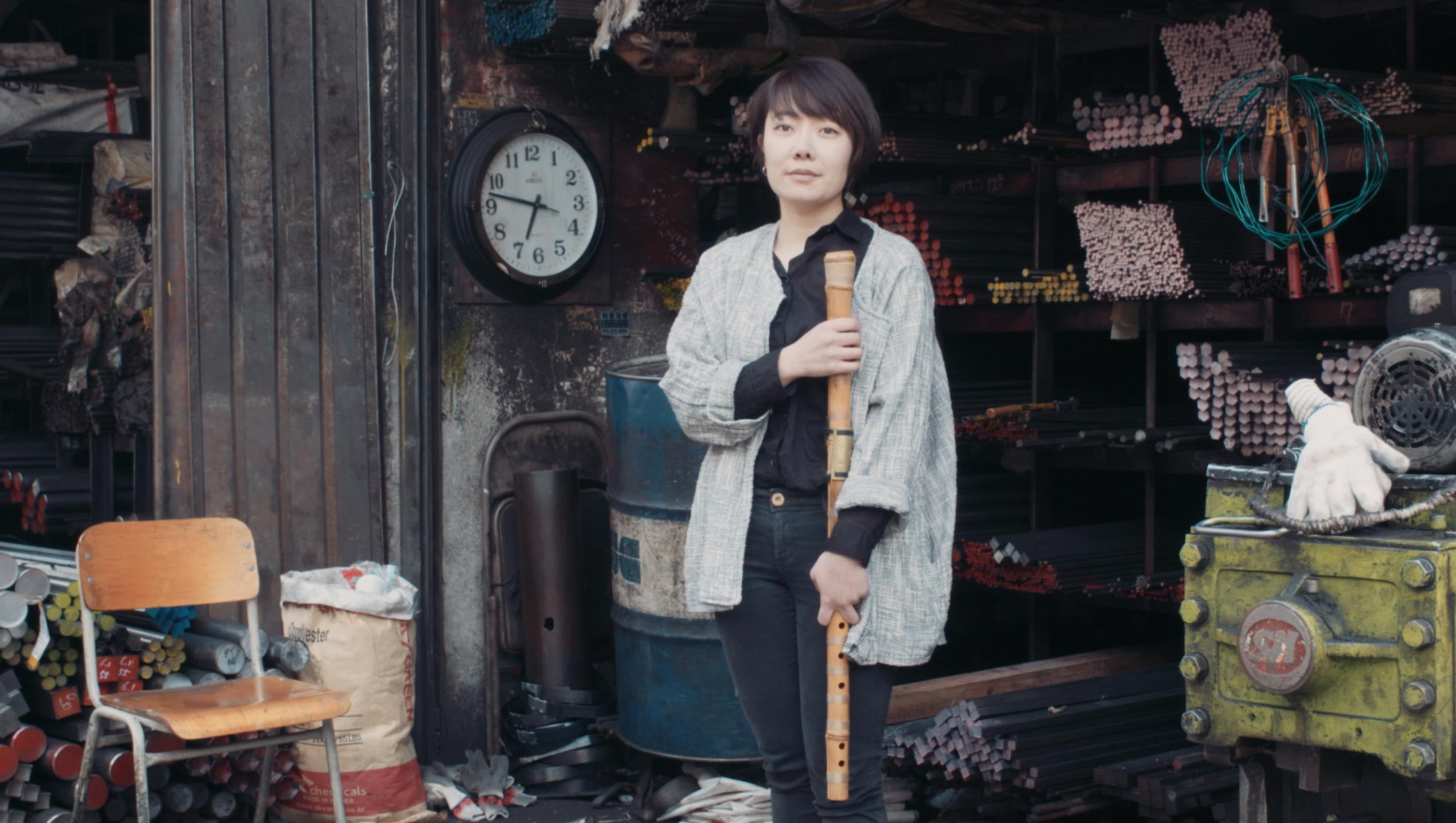 Korean musician Seungmin Cha holding traditional instrument inside metal workshop setting during Goethe Institut Seoul promo film focused on culture craft and sound