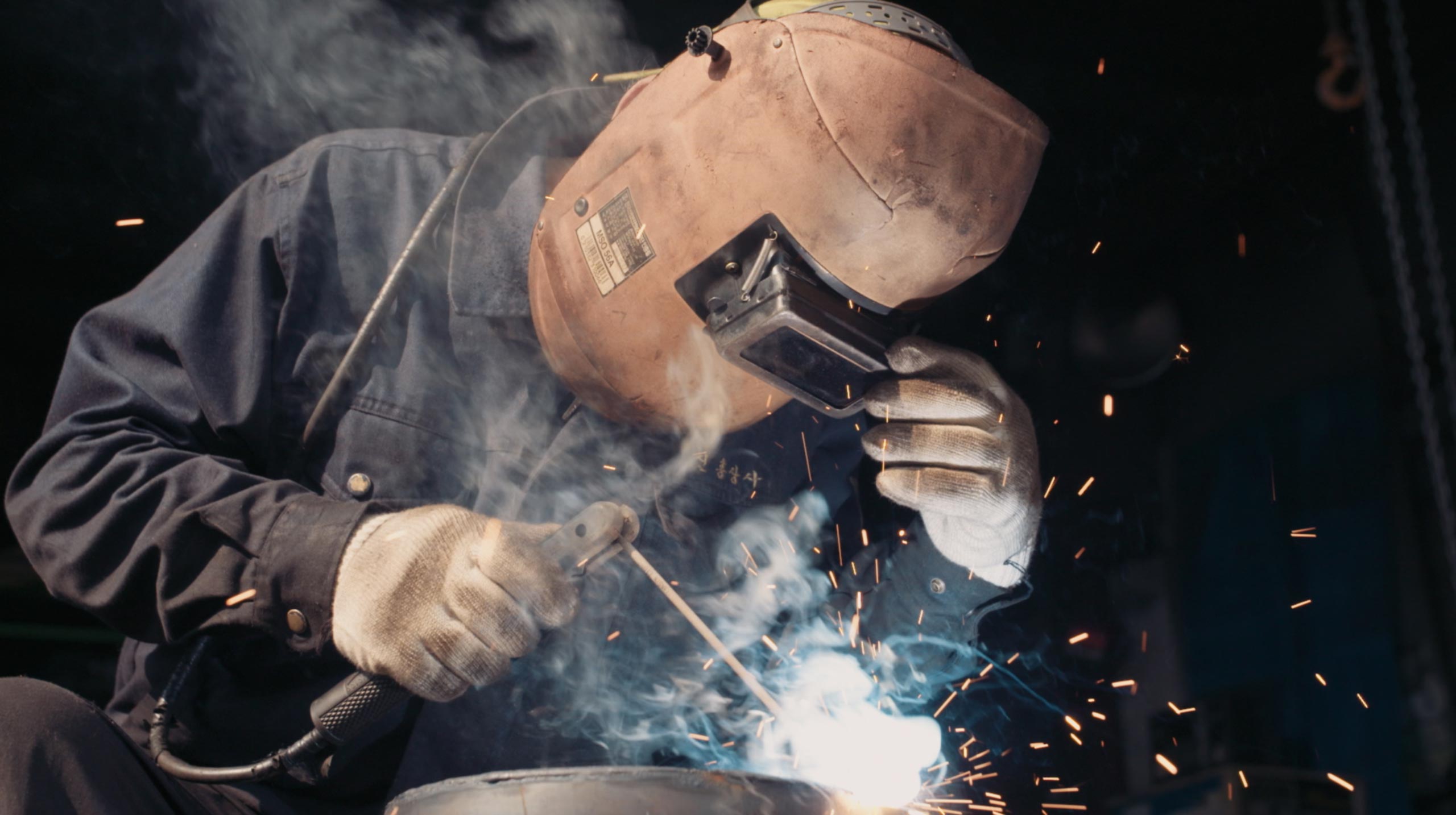 Metal worker welding steel inside industrial workshop during Goethe Institut Seoul promo film highlighting craft labor process and everyday work culture in Seoul