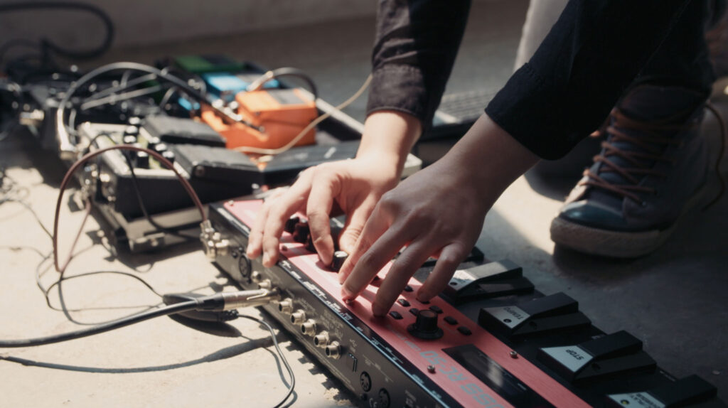 Musician hands adjusting effects pedals during sound preparation for Goethe Institut Seoul promo film focused on experimental music process and live performance