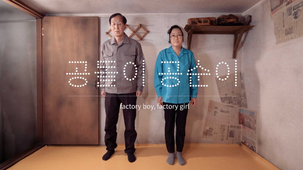 Former factory workers standing inside small domestic room representing working class life during Korean industrial expansion of 1970s and 1980s