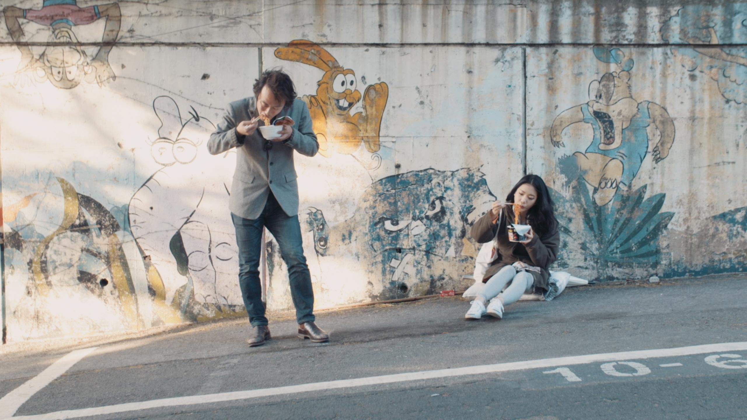 Gyungsung Lee and Korean actress sharing street meal in Seoul during Goethe Institut Seoul promo film reflecting everyday life urban culture and casual human interaction