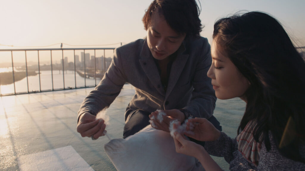 Gyungsung Lee and Korean actress examining material on rooftop in Seoul during Goethe Institut Seoul promo film focusing on shared curiosity everyday detail and interaction