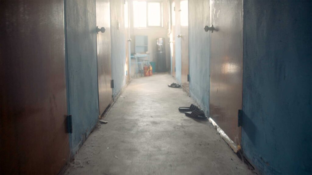 Empty factory dormitory corridor with worn doors and personal shoes reflecting daily life and living conditions of Korean industrial workers