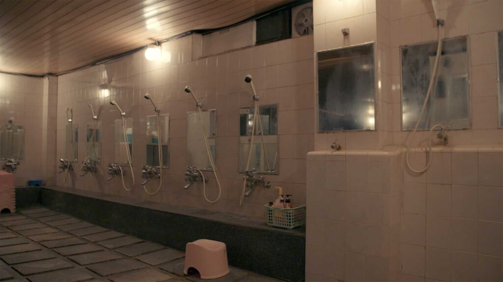 Empty communal bathhouse with tiled walls mirrors and shower heads reflecting shared routines and collective living conditions of industrial workers in South Korea