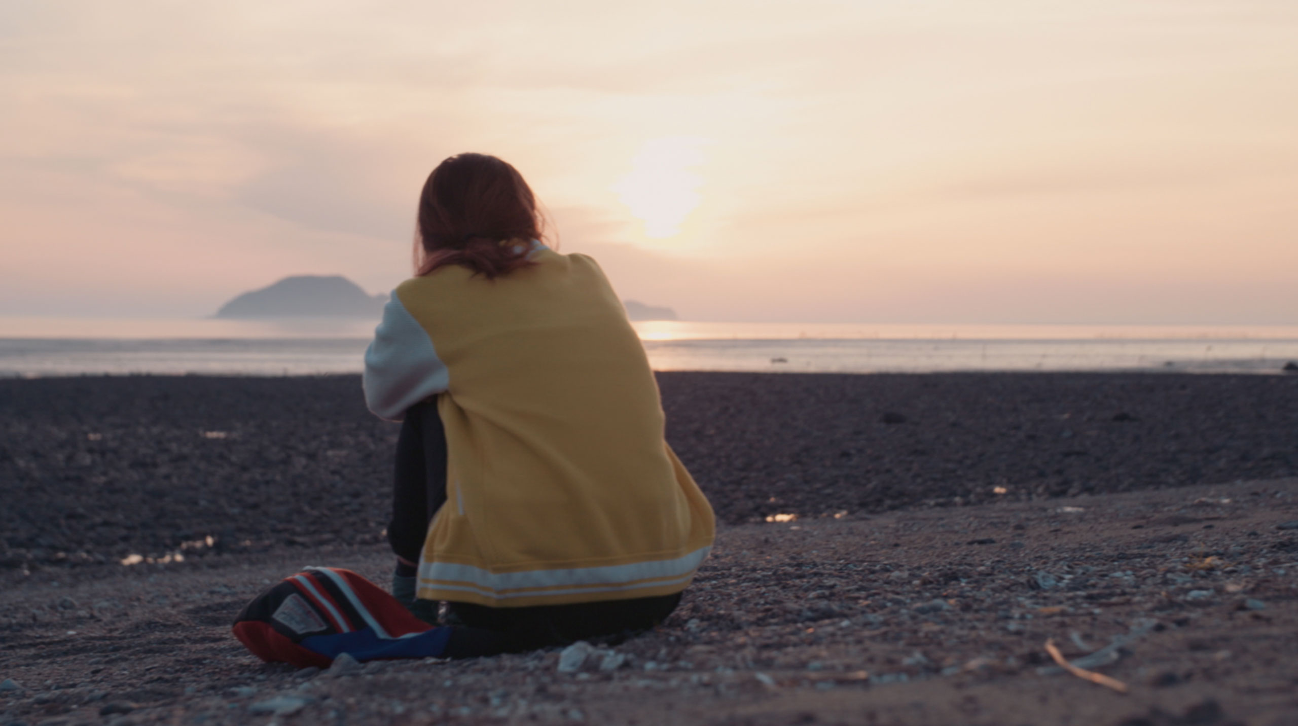 Korean actress Kkobbi Kim sitting on beach at sunset during Goethe Institut Seoul promo film reflecting pause distance and quiet observation of everyday landscape