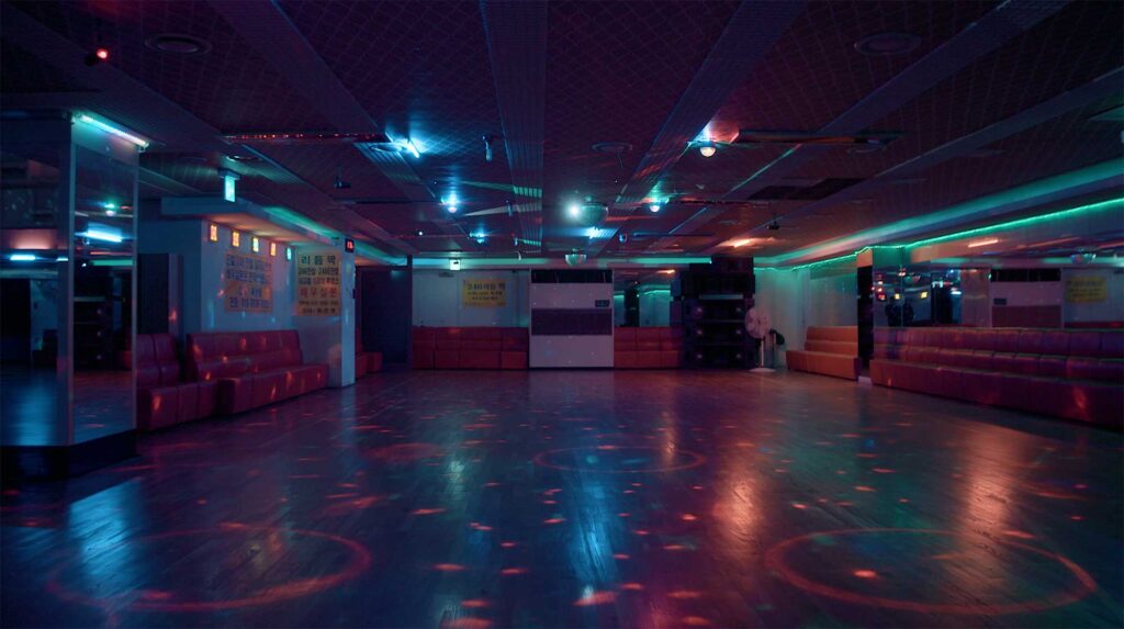 Empty dance hall with colored disco lighting reflecting on floor suggesting temporary escape and collective leisure within industrial era worker culture